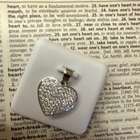 Heart-shaped earring on a white stand with a dictionary page background