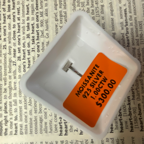 White jewelry box with a silver heart-shaped object and orange label on a printed background