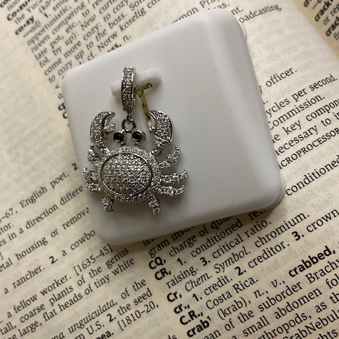 Silver crab-shaped ring on a white stone surface with text in the background