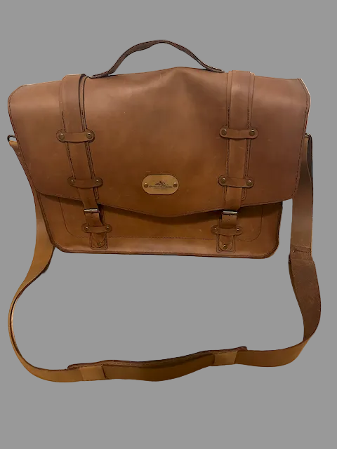 Brown leather satchel bag on a wooden floor with a white wall background