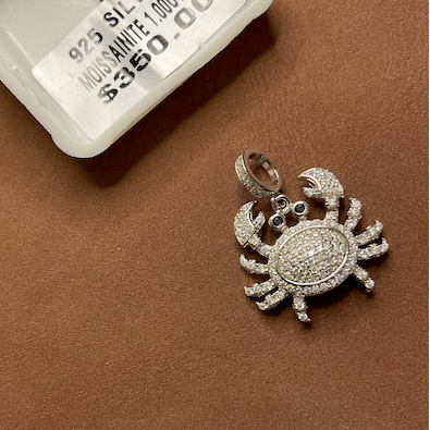Silver crab-shaped pendant on a brown surface with a white container labeled 'Silver' in the background.