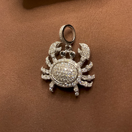 Silver crab pendant with moissanite stones on a brown surface, price tag visible.