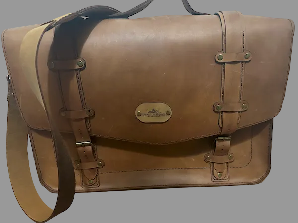 Brown leather satchel bag with a visible brand logo on a wooden floor.