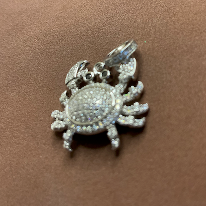 Silver crab-shaped pendant with clear stones on a brown surface