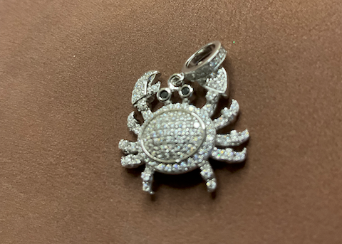 Silver crab-shaped charm with clear stones on a brown surface