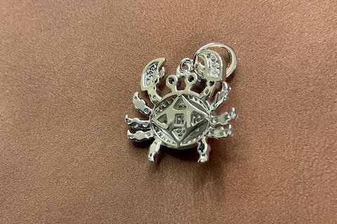Silver crab-shaped pendant on a brown surface