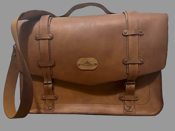 Brown leather satchel bag on a wooden floor with a white wall background